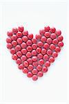 close-up of red pills arranged into heart shape on white background