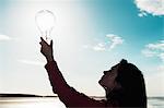 Woman holding light bulb in sky