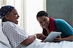 Daughter visiting mother in hospital, showing her digital tablet