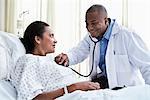 Male doctor checking female patient with stethoscope