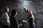 Woman writing on blackboard, colleagues watching