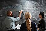 Man writing on blackboard, colleagues watching