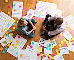 Colleagues sitting cross legged on floor with papers and adhesive notes