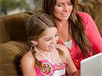 Mother and daughter using laptop on sofa