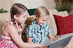 Children using laptop together on sofa