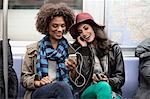 Women sharing earphones on subway