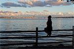 Silhouette of woman sitting on fence