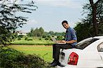 Businessman sitting on his car and using a laptop