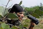 Soldier holding binoculars in a forest