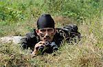 Soldier lying in a forest with binoculars