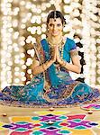 Woman greeting in prayer position near rangoli at Diwali festival