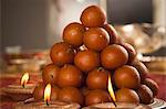 Candles burning around a tray of gulab jamuns