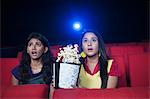 Two female friends looking surprised while watching movie in a cinema hall