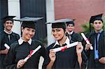 Portrait of graduate students holding diplomas and smiling in university campus