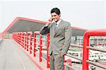 Businessman standing on a footbridge and talking on a mobile phone, Gurgaon, Haryana, India