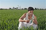 Farmer crouching in the field and smiling, Sonipat, Haryana, India