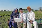 Businessman sitting in the field near his parents and using a laptop, Sonipat, Haryana, India