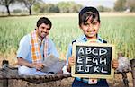 Schoolgirl showing a slate with his father sitting in the background, Sohna, Haryana, India