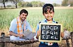 Schoolgirl showing a slate with his father sitting in the background, Sohna, Haryana, India