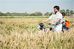 Farmer with his daughter riding a motorcycle in the field, Sohna, Haryana, India