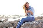 Young Woman Sitting on Rocks and Texting on Cell Phone at Beach, Jupiter, Palm Beach County, Florida, USA