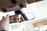 Man looking in an interior car mirror while sitting in a car