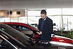 Man writing on a clipboard beside a car in a garage