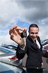 happy dealer holding car keys by his fingertips outddors