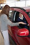 Businesswoman presenting the car to a client in a dealership