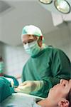 Patient sleeping on a surgical table while a surgeon is taking scissors in a surgical room