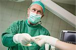 Smiling surgeon taking a tool from a gloved hand in a surgical room