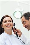 Doctor using an otoscope to look at the ear of a patient in an examination room