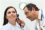 Doctor using an otoscope to look at the ear of his patient in an examination room