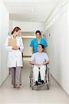 Nurse pushing a patient in a wheelchair while talking to a doctor in a hospital hallway