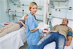 Two patients lying on bed next to a nurse in hospital ward