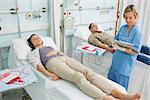 Nurse next to a transfused patient writing on a clipboard in hospital ward