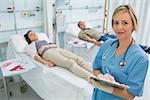 Nurse next to transfused patients writing on a clipboard in hospital ward