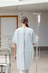 Rear view of a female patient holding a drip stand in hospital corridor