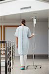 Rear view of a patient holding a drip stand in hospital hallway