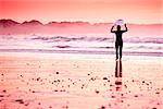 Female surfer on the beach at the sunset