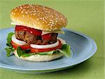 Photo of a hamburger on a blue plate resting on a green table cloth.