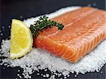 Photo of a raw salmon steak with thyme, lemon slice, on a bed of sea salt and black slate.