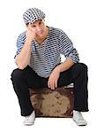 Sad waiting young male traveler siting on old vintage suitcase isolated on white background