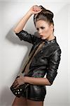 very young sexy brunette with leather jacket, shorts and bag with hair style near a wall