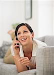 Happy young woman laying on couch and talking cell phone