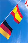 English, Spanish, and German flags against blue summer sky