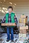 Boy holding Christmas gifts on snowy porch