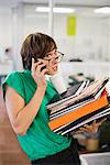 Businesswoman with folders talking on cell phone