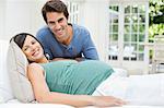 Man sitting next to pregnant woman resting on bed