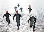 Triathletes in wetsuits running into ocean